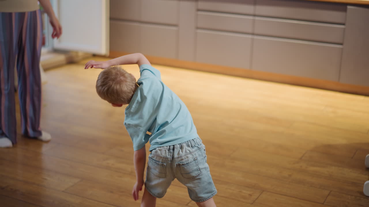 Young boy in blue shirt and shorts playing actively on wooden floor, supporting body with hands in dynamic playful motion, expressing energy, joy, childhood activity and fun at home environment