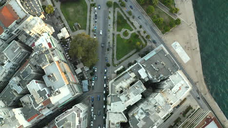 Topdown-aerial-drone-shot-of-the-greek-city-of-Thessaloniki-with-moving-cars-along-a-road-next-to-the-sea-with-the-iconic-white-tower-of-Thessaloniki-at-sunset-in-4k