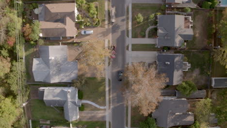 overhead view of suburban neighborhood in autumn as a car drives down the street and pulls into a driveway