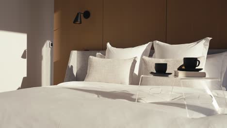 a luxury bedroom with a large white king bed and a bed side table on it which includes 2 black coffee mugs and a book