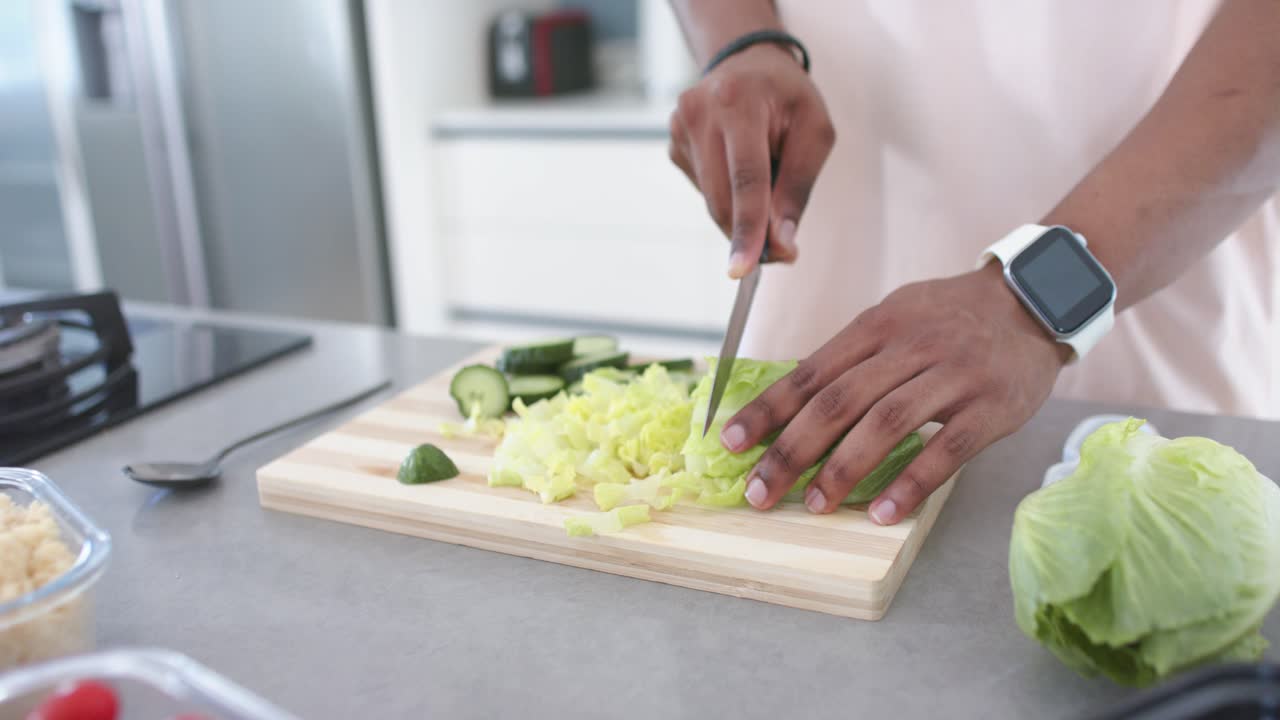 Afroamerikanischer Mann beginnt mit der Salatzubereitung, schneidet Salat mit einem Messer auf einem Schneidebrett in der Küche.