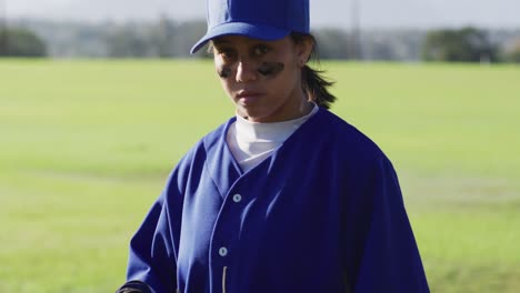 portrait of mixed race female baseball player wearing eye black, throwing ball into glove