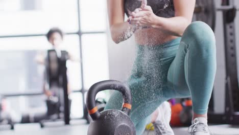 Video-of-confident-caucasian-woman-powdering-hands-before-working-out-with-kettlebell-weight-at-gym