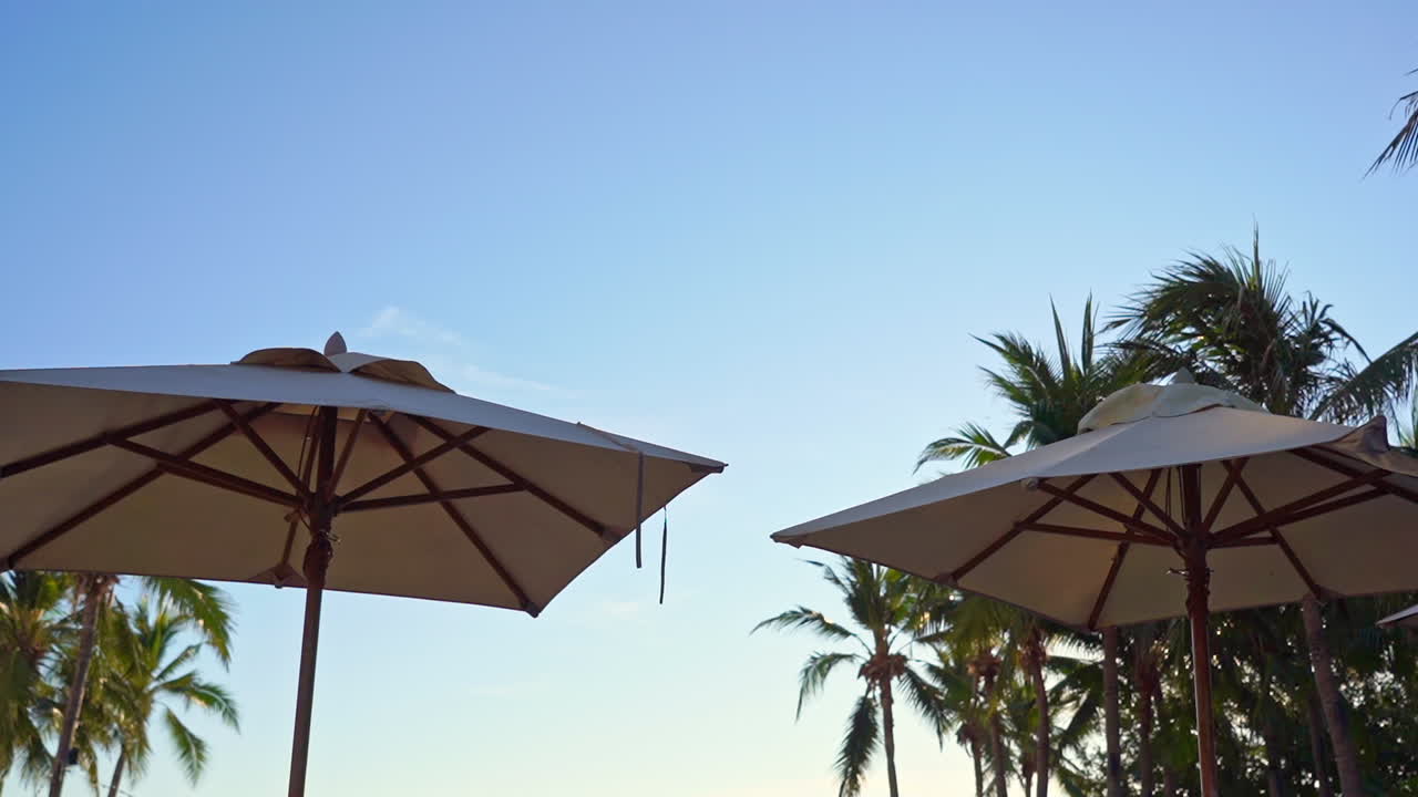 A relaxing and peaceful scene of two hotel umbrellas on a clear blue sky during a sunny day