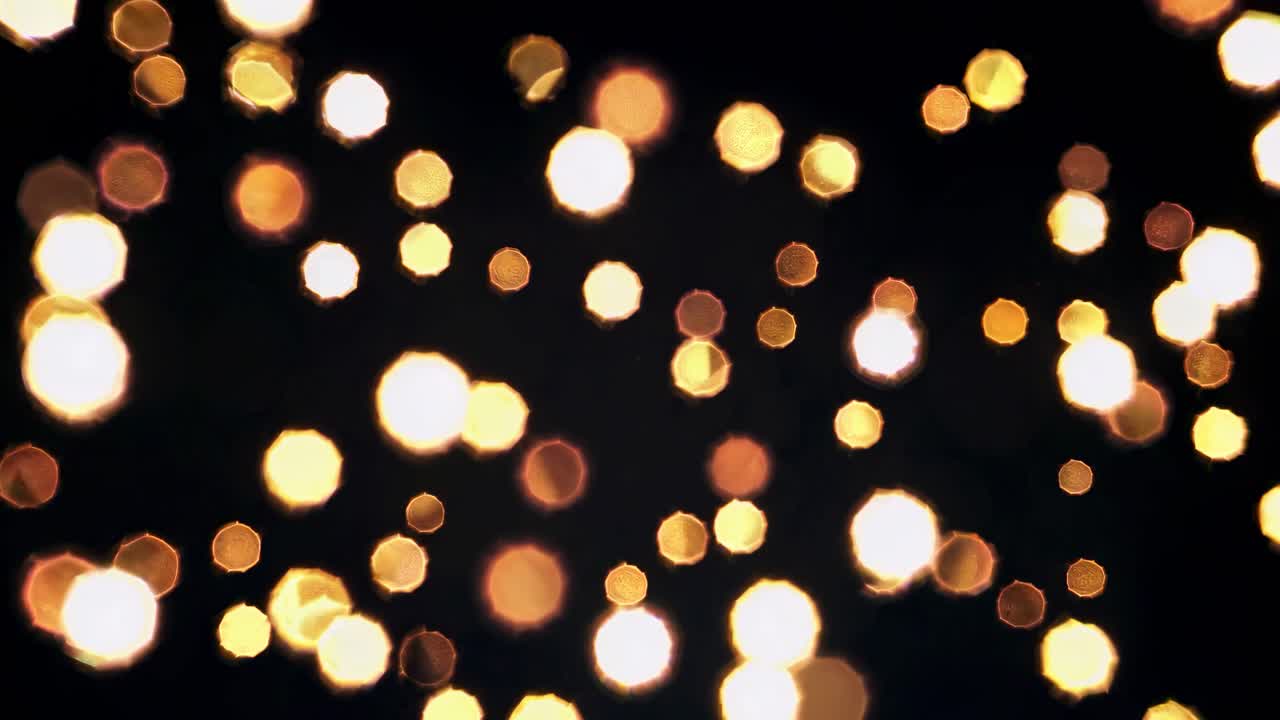 Un video ipnotizzante di luci bokeh dorate su uno sfondo scuro, ripreso frontalmente.