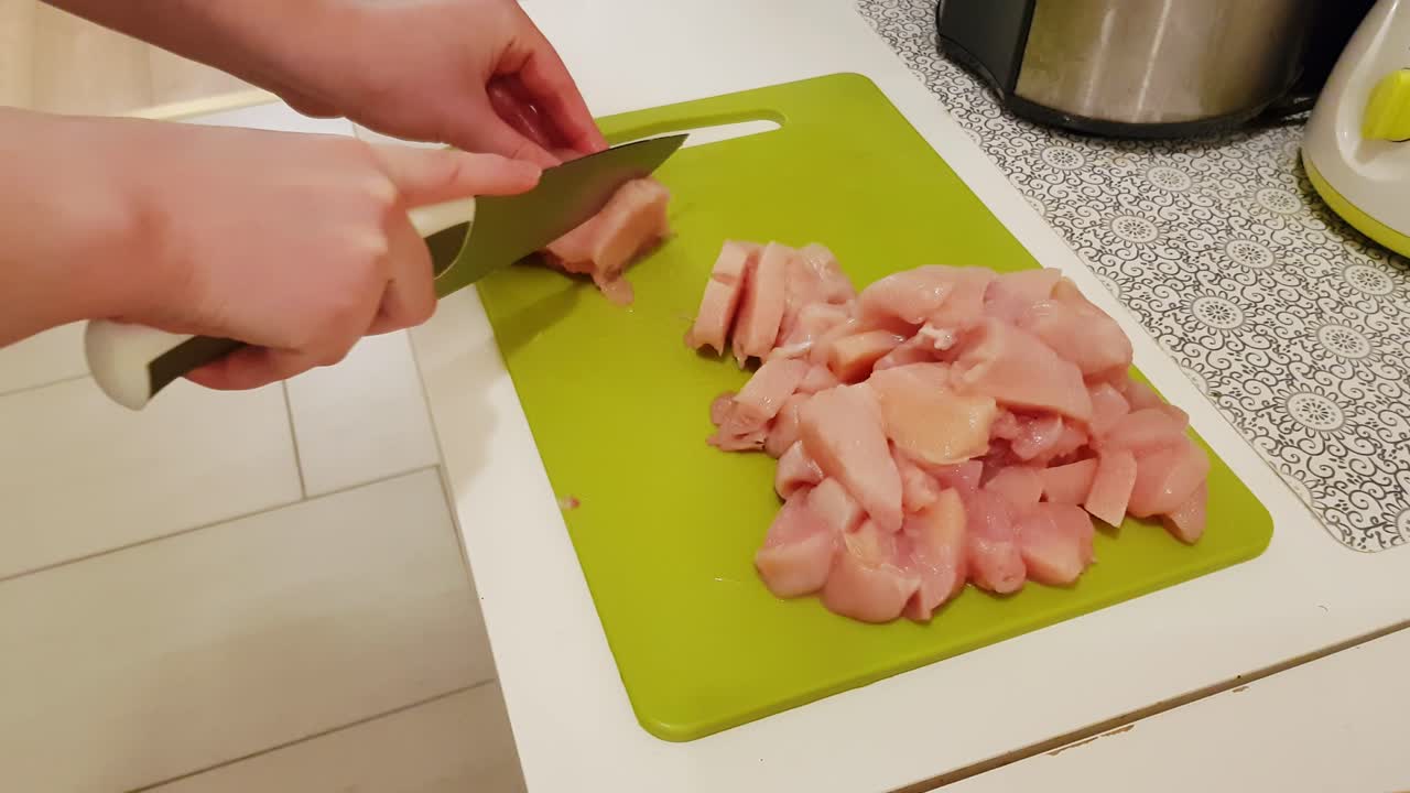 mujer caucásica cocinando y cortando carne de pechuga de pollo cruda