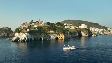 drone panning shot of a sailing boat passing grotta di pilato on isola di ponza on a sunny day