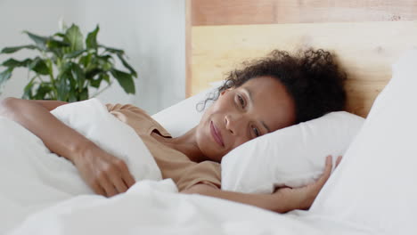 woman waking up in bed, smiling and stretching, enjoying morning relaxation, at home