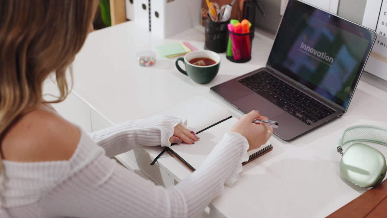 Woman working on laptop and writing in notebook