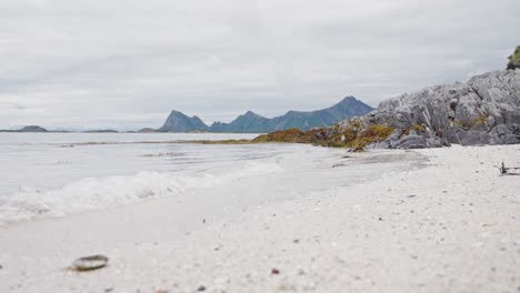 ruhige wellen durch weißen sandstrand mit felsigen bergen im hintergrund im sommer in norwegen