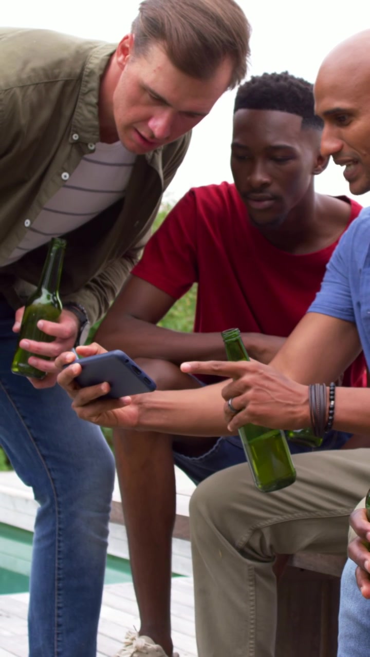 Vertical video: Showing seated man sharing smartphone with friends at pool deck, holding beers