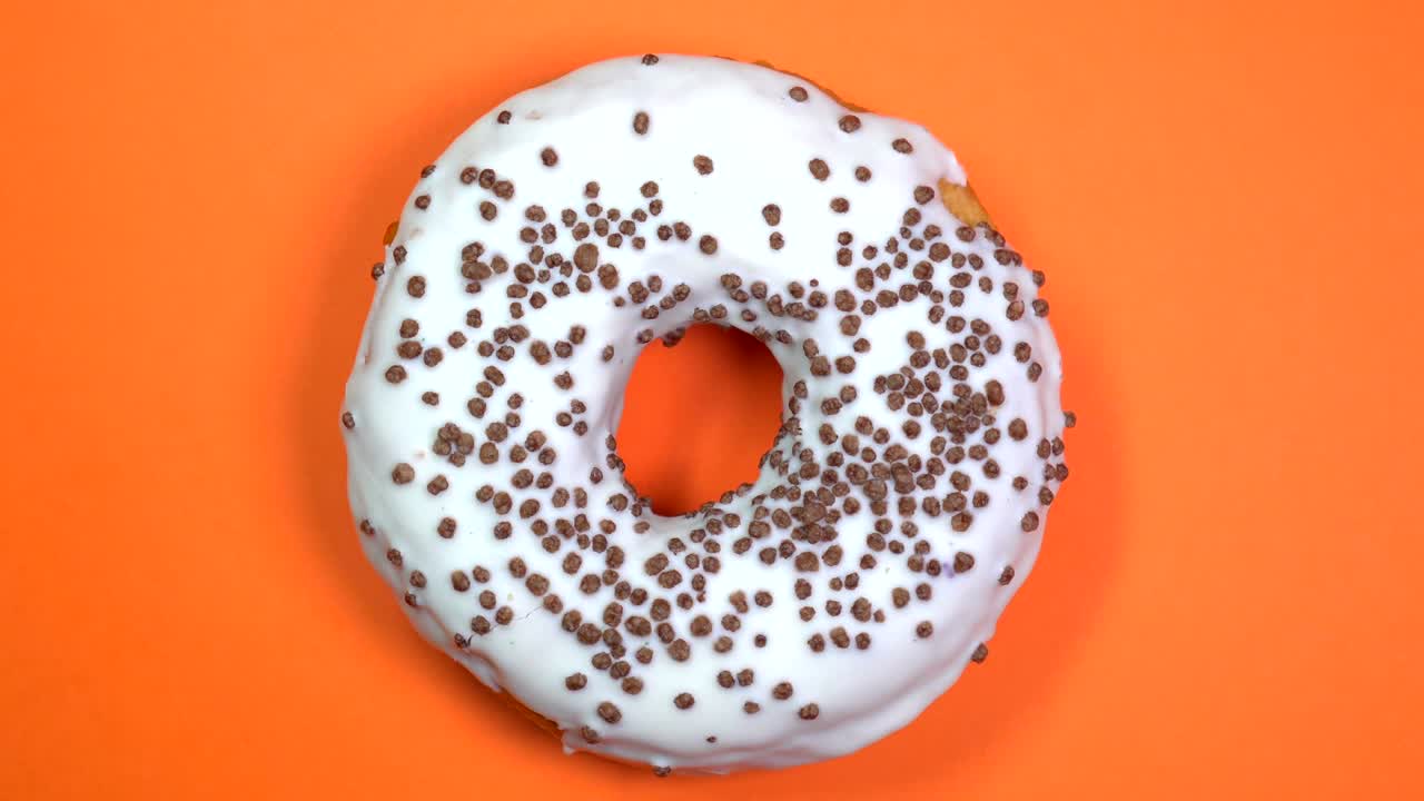 donut brillante y blanco con bolas de chocolate, macro disparado, girando sobre un fondo naranja.