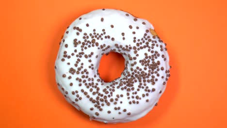donut brillante y blanco con bolas de chocolate, macro disparado, girando sobre un fondo naranja.