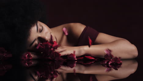 portrait beautiful african american woman with afro red rose petals blowing sensual female looking seductive dreaming of intimate fantasy romance indulging desire in valentines day concept