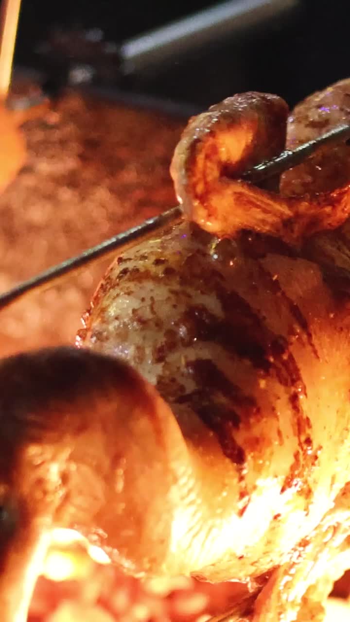 A whole duck rotates on a metal skewer over intense orange flames and hot charcoal