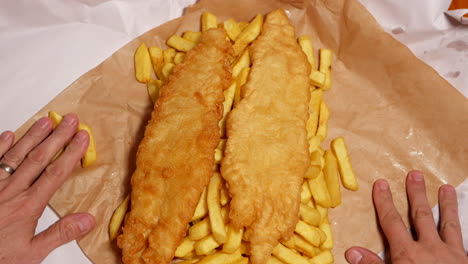 el hombre abre un envoltorio de papel con pescado y patatas fritas dentro