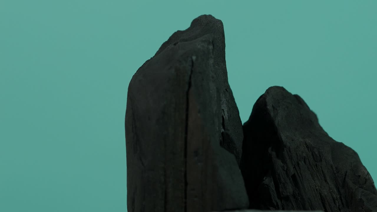 древесный уголь. черный уголь на синем зеленом фоне. используется для приготовления пищи на гриле или в промышленности. естественный древесный углерод. черный углерод, полученный при сильном нагревании древесины.