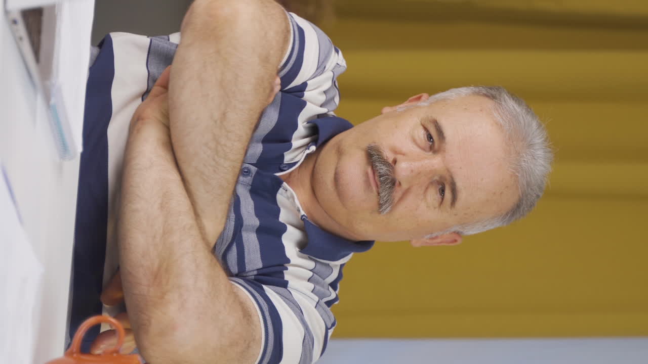 vídeo vertical de un anciano trabajador de oficina en casa hace una señal de confianza a la cámara.