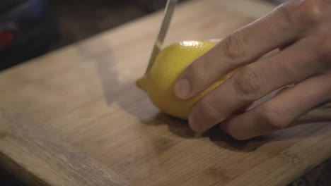 a person hands cutting slowly a fresh ripped lemon on a cutting board - close up shot