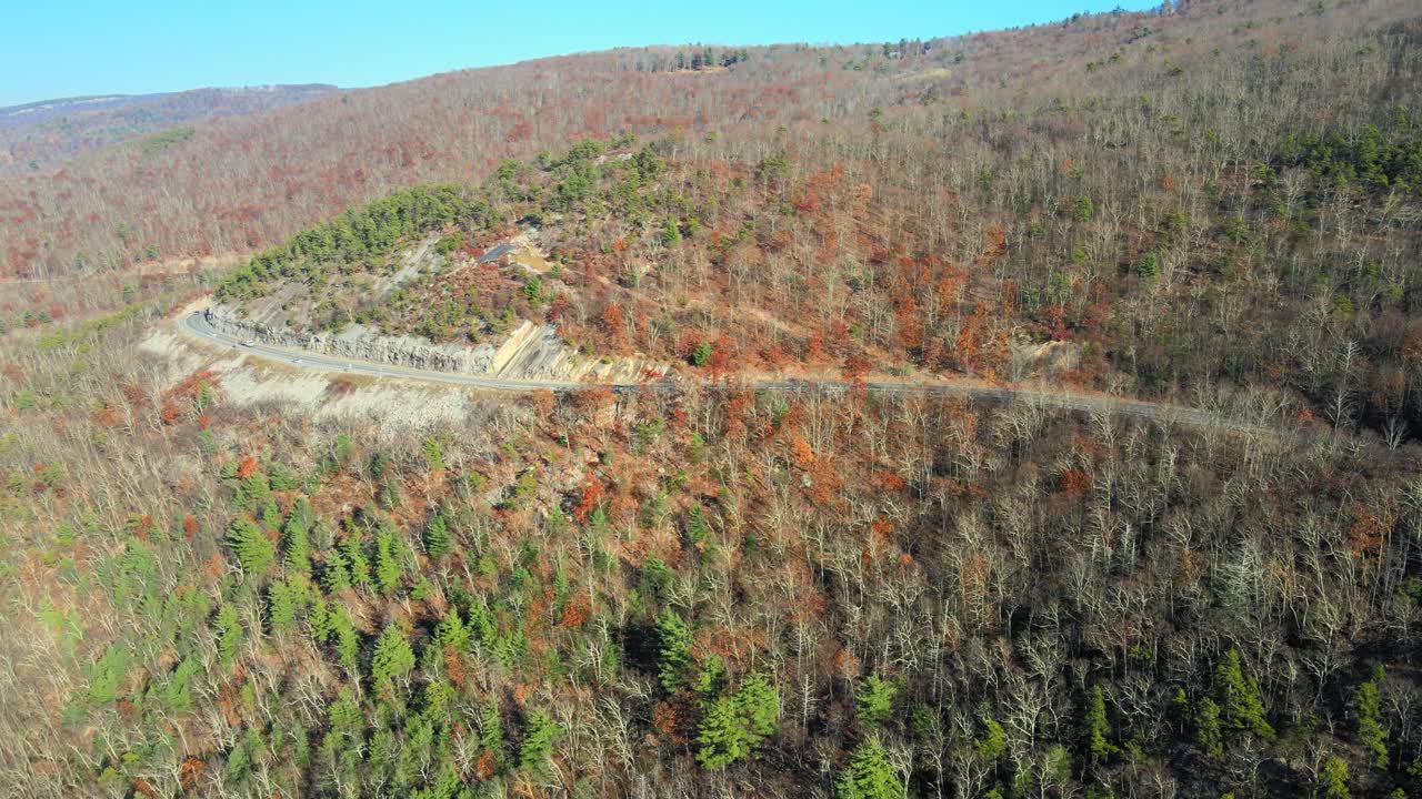 가을 동안 숲과 계곡, 아래 농지와 배경에 산이 있는 경치 좋은 산간 고속도로의 드론 영상