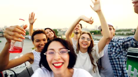 point of view shot of cheerful young lady recording video of her friends multiracial group dancing at open-air party having fun and laughing looking at camera.