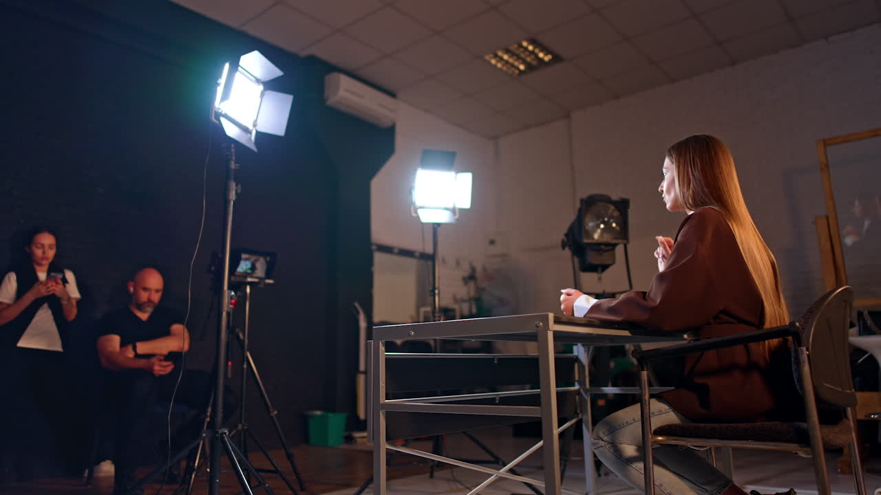 Blogging backstage in the modern studio. Camera records a female blogger talking and gesturing in the lights of soffits. Low angle view.