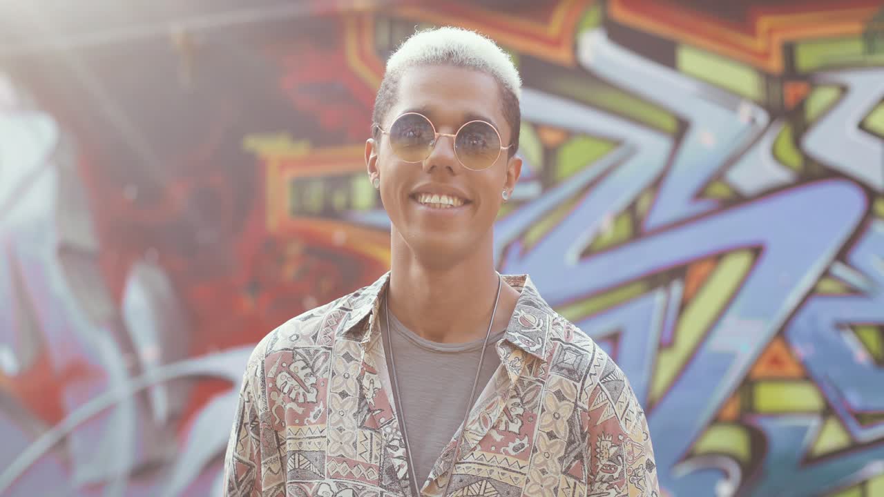 그래피티 벽에 서서 카메라를 보고 웃고 있는 젊은 백인 세련된 힙스터 남자의 초상화