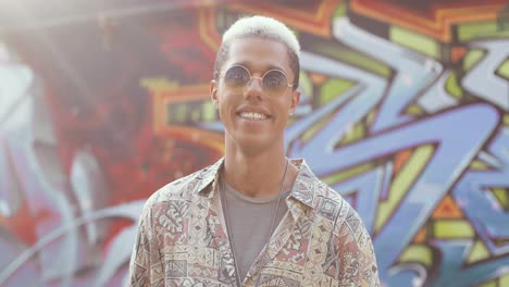 foto de retrato de un joven hipster con estilo caucásico parado en la pared de graffity y sonriendo a la cámara