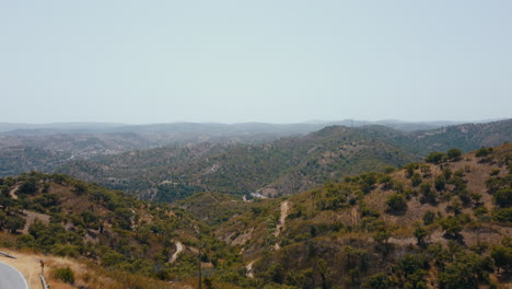 Aerial-view-showing-green-mountain-range-and-asphalt-road-on-edge-during-summer-trip-in-Algarve,Portugal