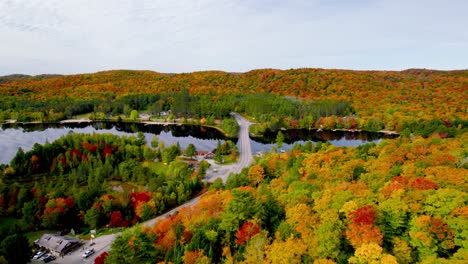Scenic-Fall-road-trip-top-down-aerial-view-through-rolling-hills-small-town-colorful-trees-and-bridge-across-a-lake