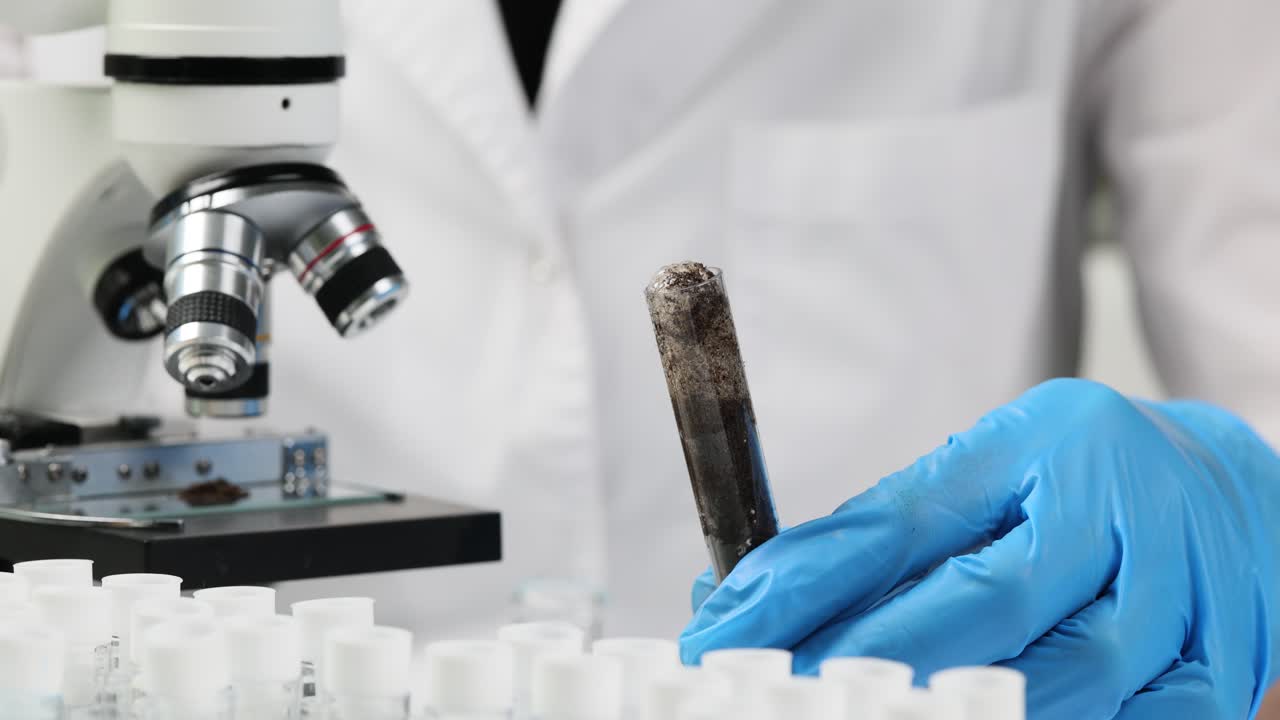 Chemist in rubber gloves holds test tube with black soil