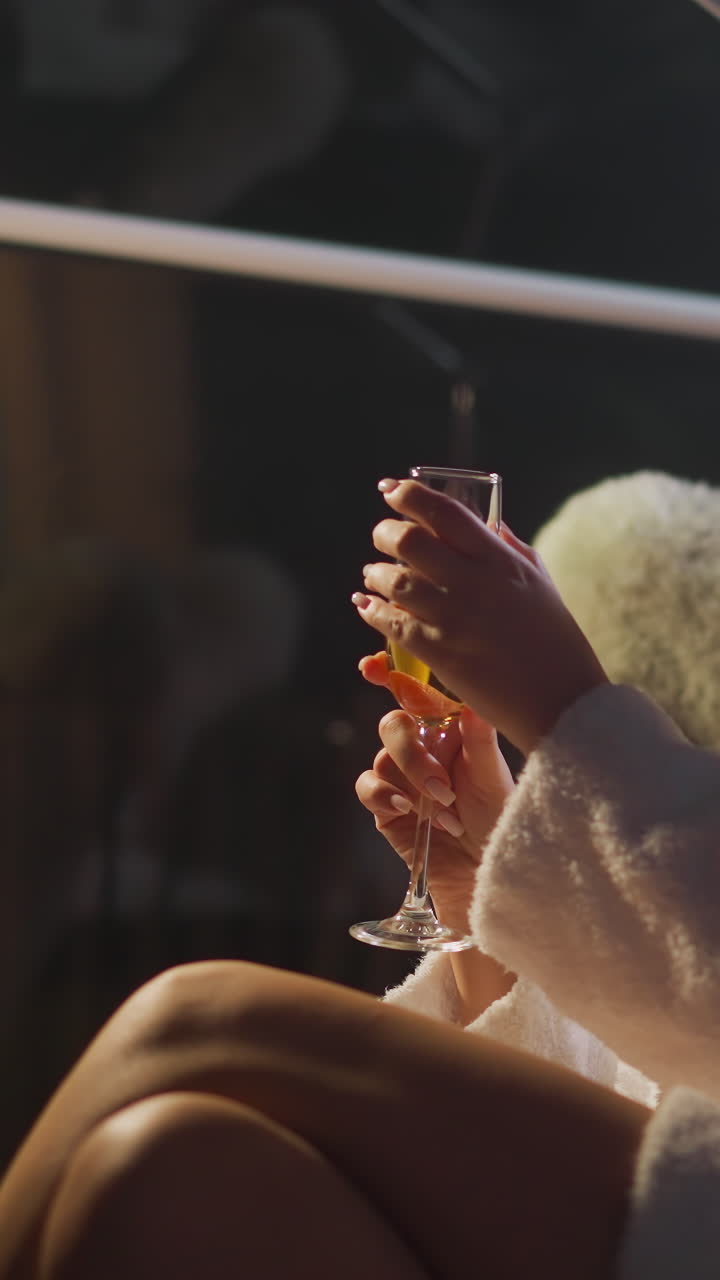 피곤한 여자가 페인 한 잔을 고 좌석에 앉아 있습니다. 여자는 자연의 야간 생활을 내려다보는 파노라마 창문으로 방에 램프 조명 아래 앉습니다.