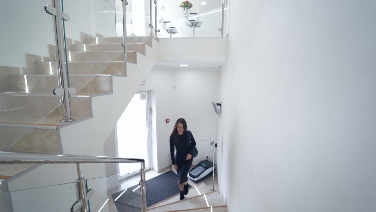 Pretty female in black dress inside the light building. Young beautiful business woman is going upstairs in a business center or in a hotel.