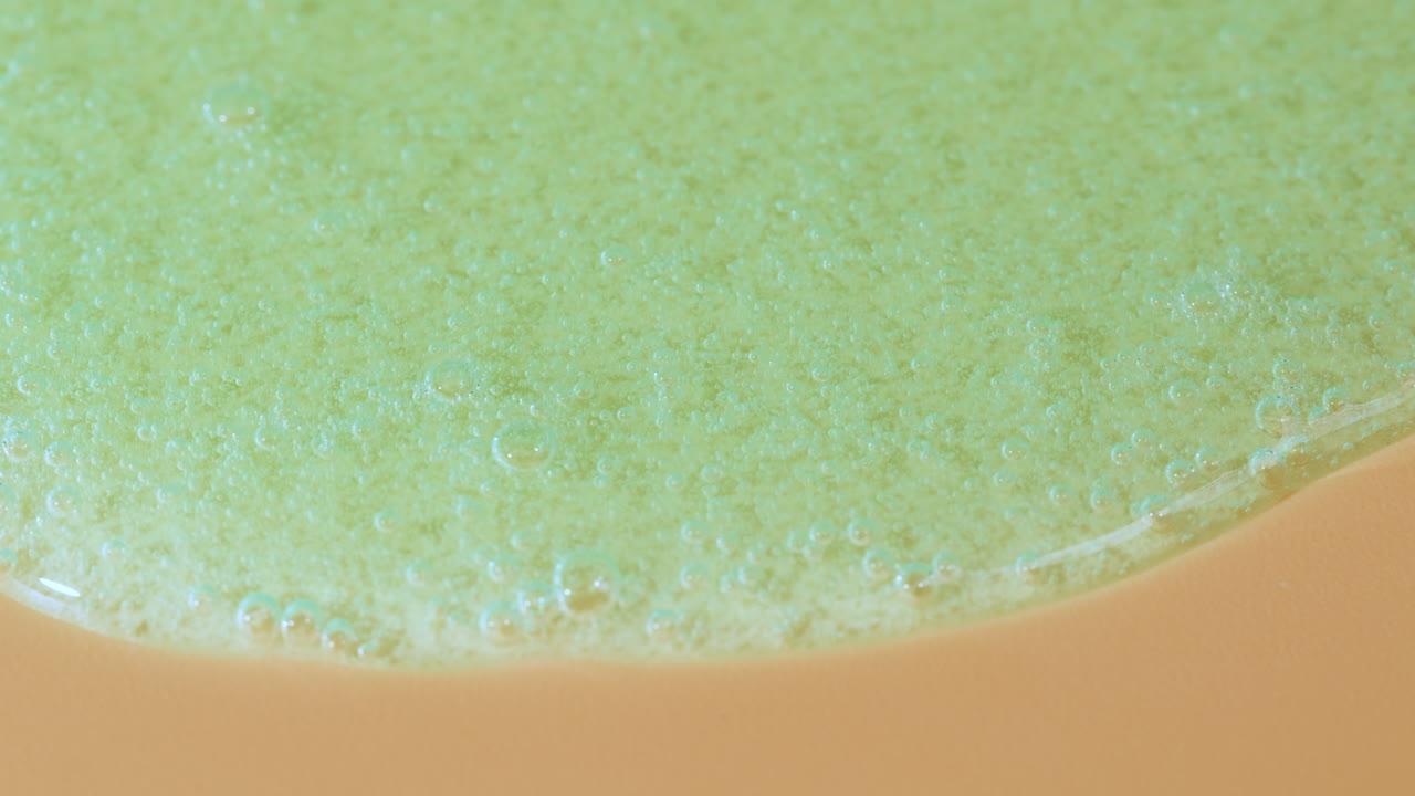 Scatto Macro di Gel Verde con Bolle che si Diffondono su Superficie Beige