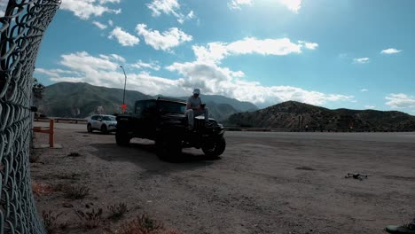 cucasian male drone pilot filmmaker sititng on hood of a jeep and lunching his drone in california