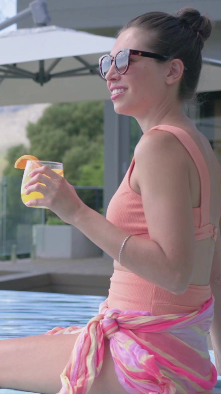 Video verticale: Donna che si allunga, solleva e sorseggia una bevanda per rinfrescarsi in piscina, bicchiere e bikini, spazio per il testo.