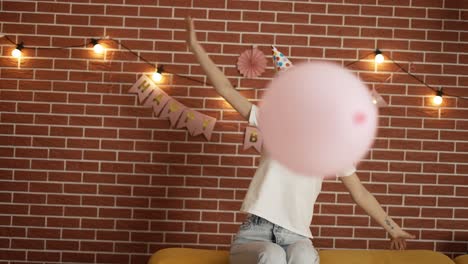 Blondy-in-birthday-hat-in-decorated-room-playing-balloon