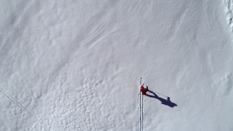 aerial top down view of a lone person skiing across a remote mountain peak, leaving the tracks of his adventure behind