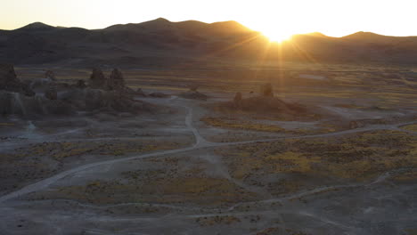 golden sun peaking over the mountains casting dramatic light over trona pinnacles in the californian desert