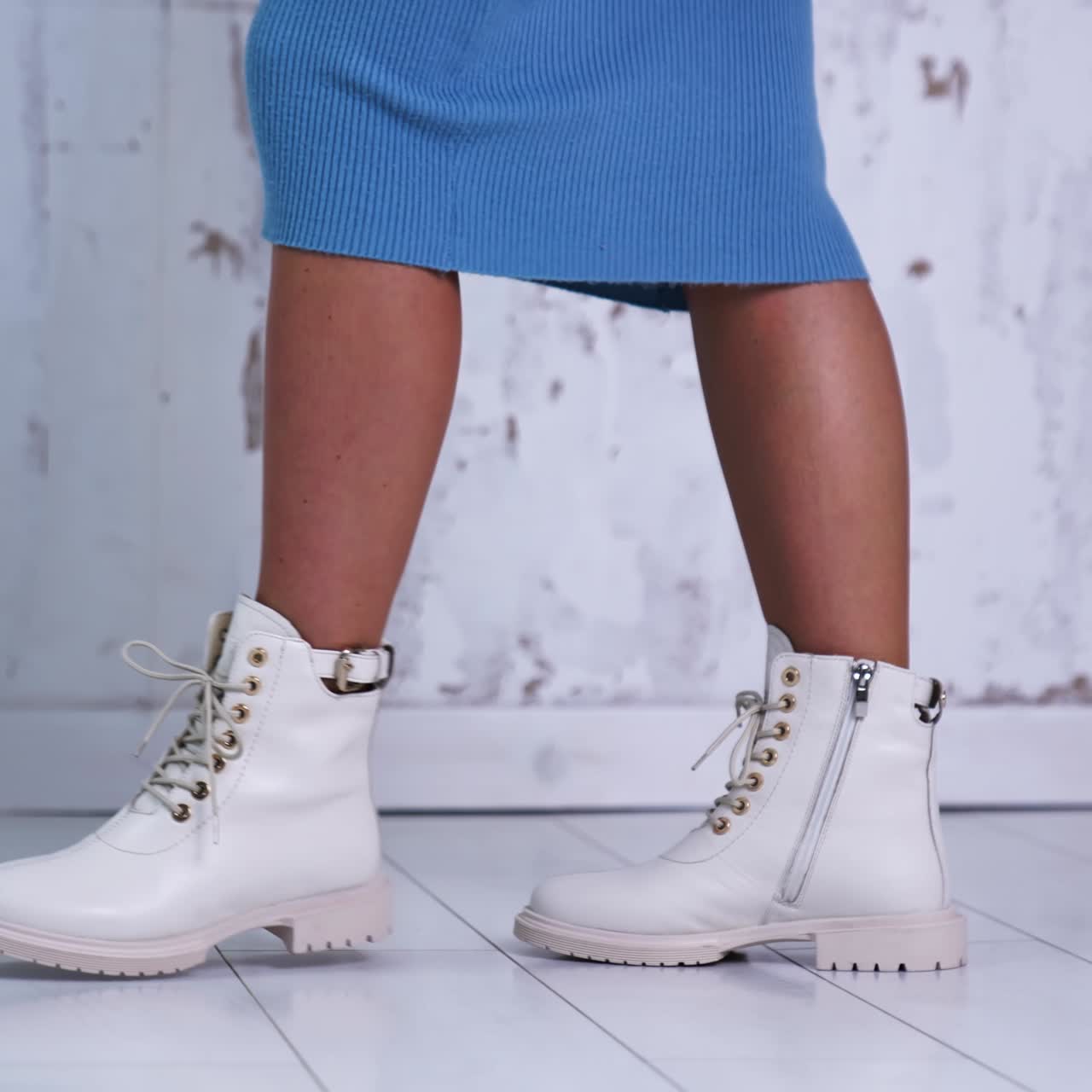 Unrecognized woman in blue dress shows the light leather boots with laces. New fashionable stylish footwear at white backdrop