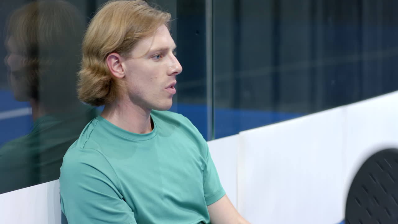 Man resting after intense padel tennis match, catching breath on indoor court bench, copy space