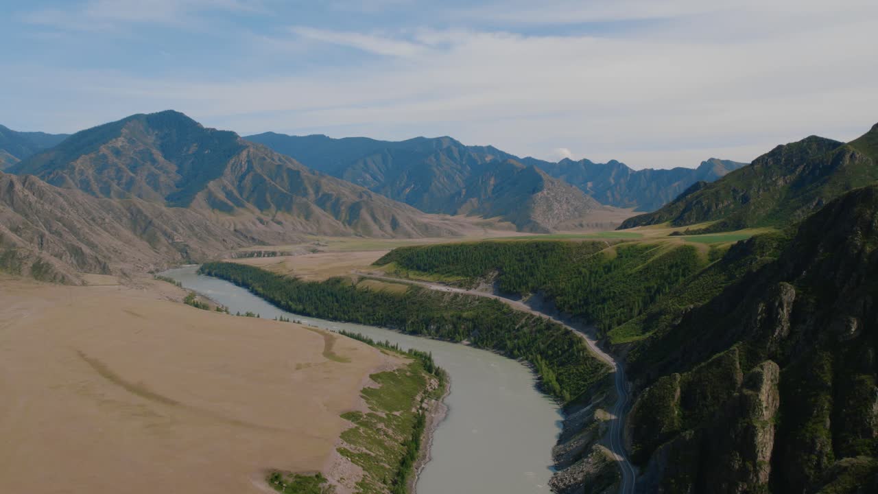Drone footage of the Katun River winding through a wide mountain valley beside the Chuysky Trakt highway in Altai Republic, Russia, under a clear summer sky