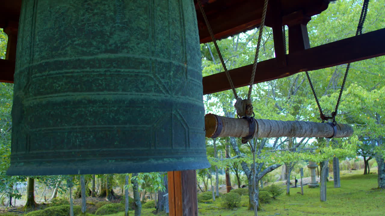 일본 교토의 아름다운 정원에 있는 나무로 둘러싸인 큰 일본 종은 부드러운 조명을 닫습니다