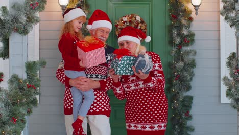 happy senior grandparents with granddaughter holding many gift boxes near christmas house, celebrate