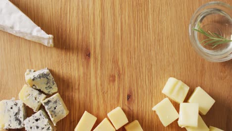 video of assorted hard and soft cheeses and rosemary in oil on wooden board with copy space