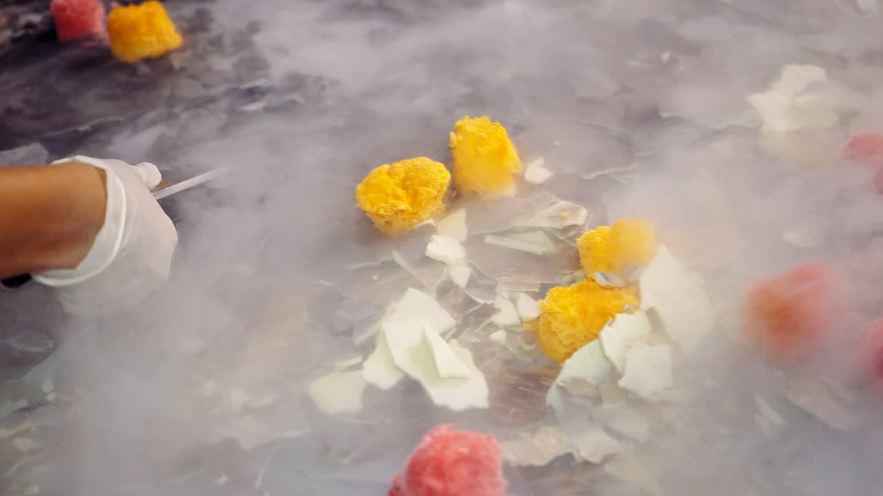 Cooks are taking pieces of cold ice cream on the white steam background. Sweet freezing ice cream with liquid nitrogen. Delicious ready ice-cream is putting on a white plate.