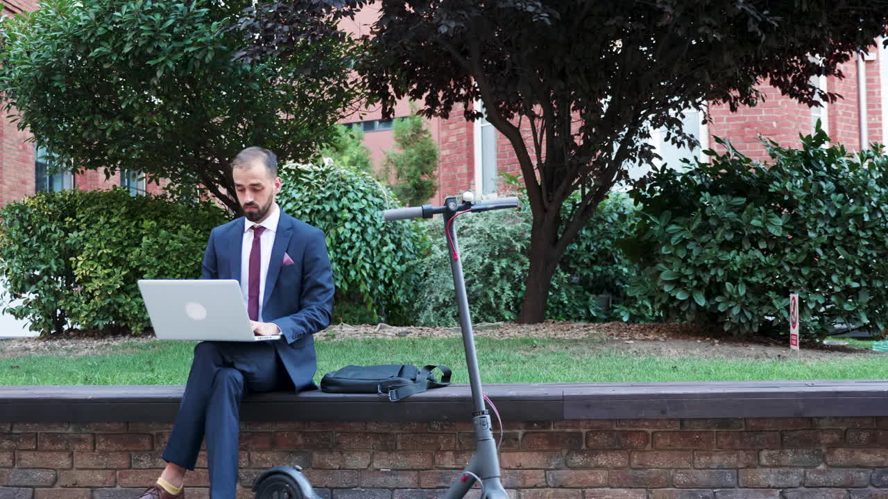 Businessman working on laptop outdoors with scooter