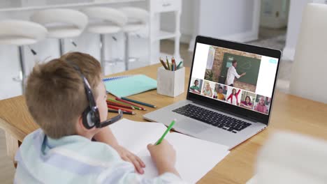 Schoolboy using laptop for online lesson at home, with diverse teacher and class on screen