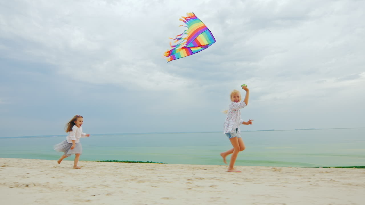 dos niñas jugando en la playa volando una cometa