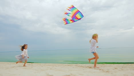 Two-Little-Girls-Playing-On-The-Beach-Flying-A-Kite